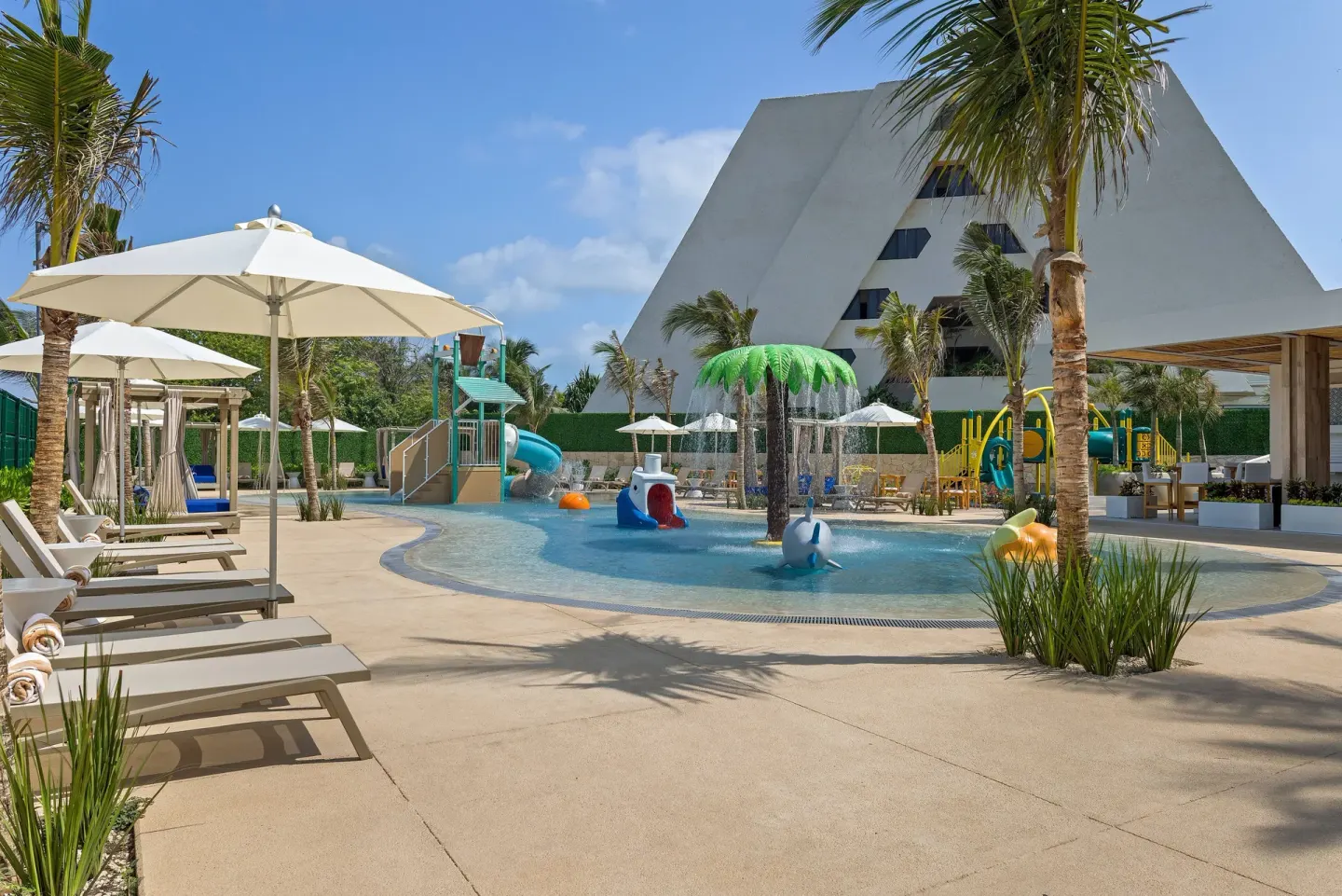 Splash pool at Wyndham Grand Cancun Resort & Villas with loungers, umbrellas, and palm trees.