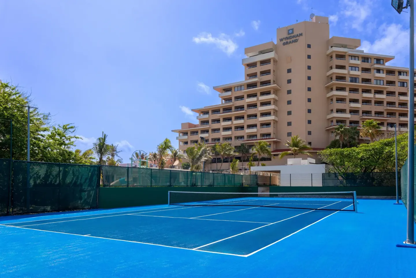 Blue tennis court at Wyndham Grand Cancun Resort & Villas with the hotel tower in the background.
