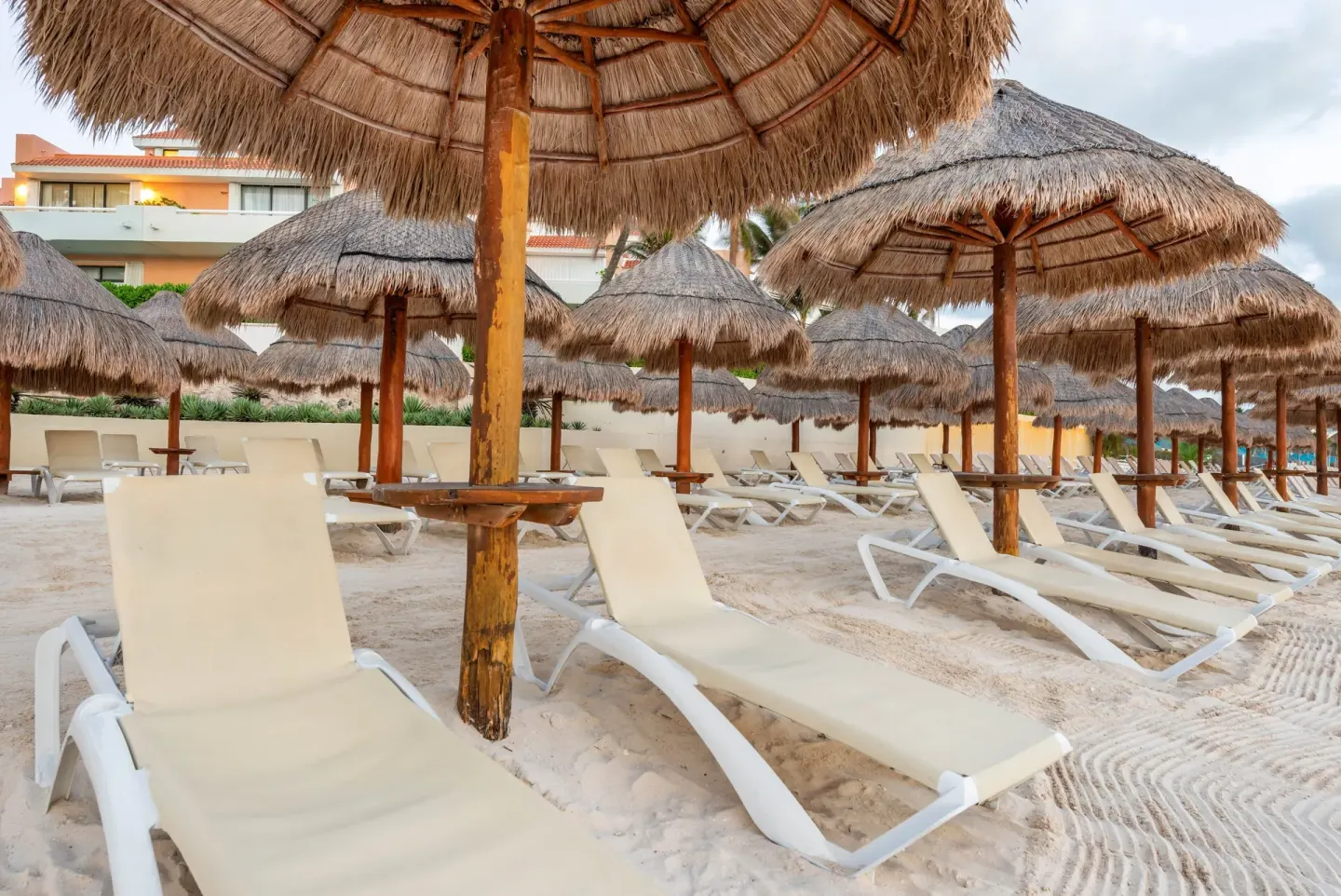 Beach loungers under thatched umbrellas at Wyndham Grand Cancun Resort & Villas.
