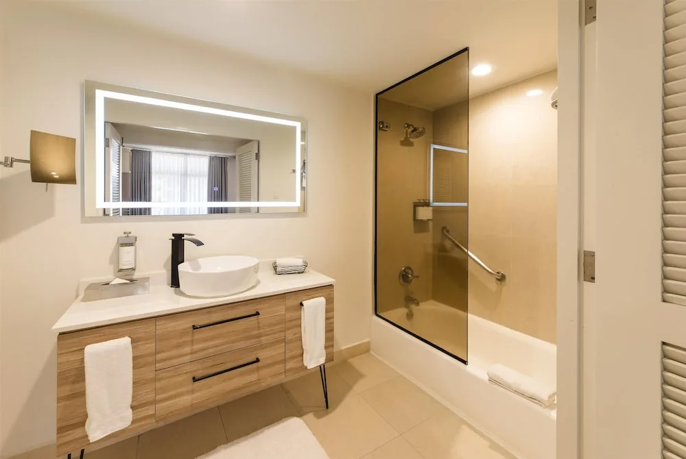 Bathroom with lighted mirror, vanity, and tub shower at Wyndham Palmas Beach and Golf Boutique Resort.