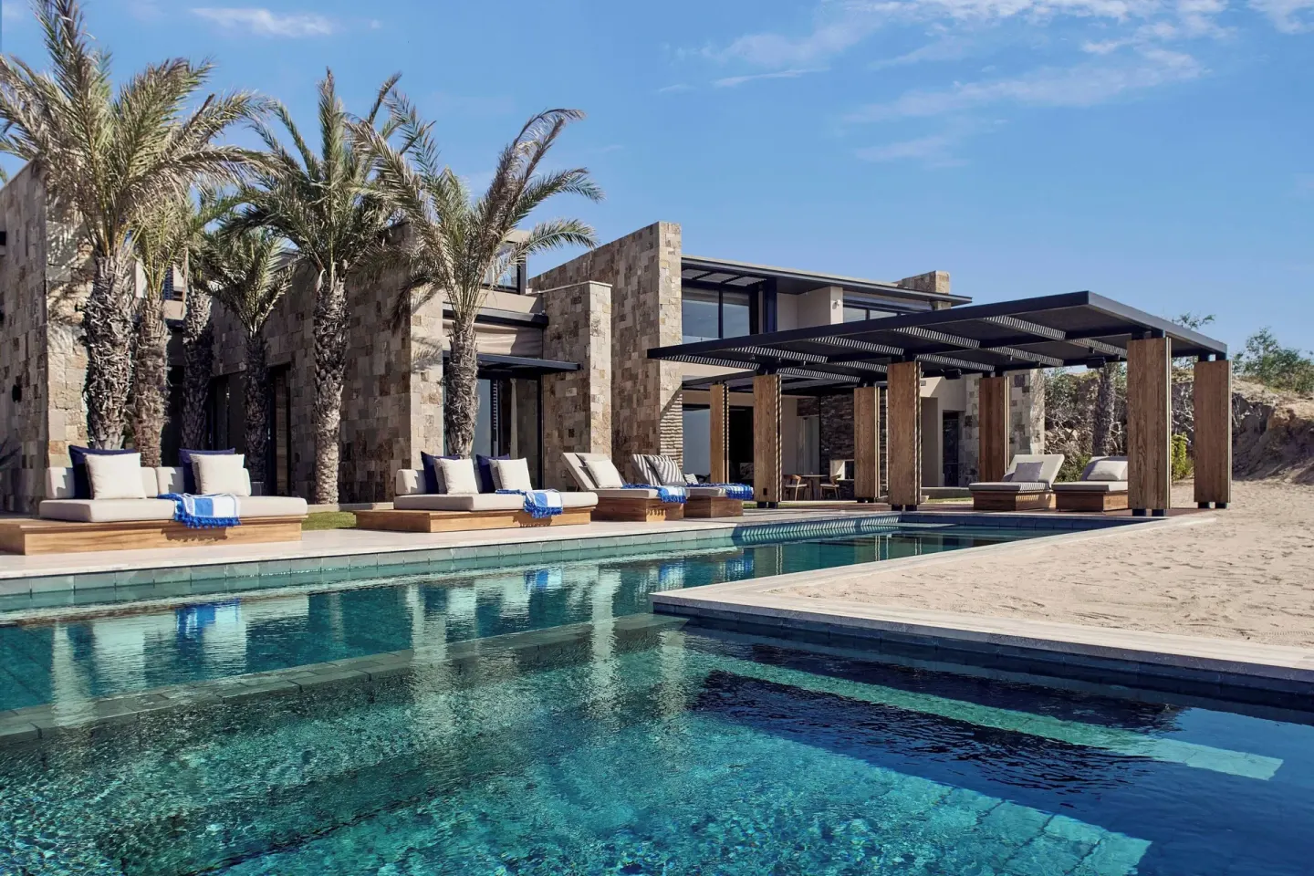 Resort pool with cabanas, palms, and stone buildings at Zadún, a Ritz-Carlton Reserve, Los Cabos.