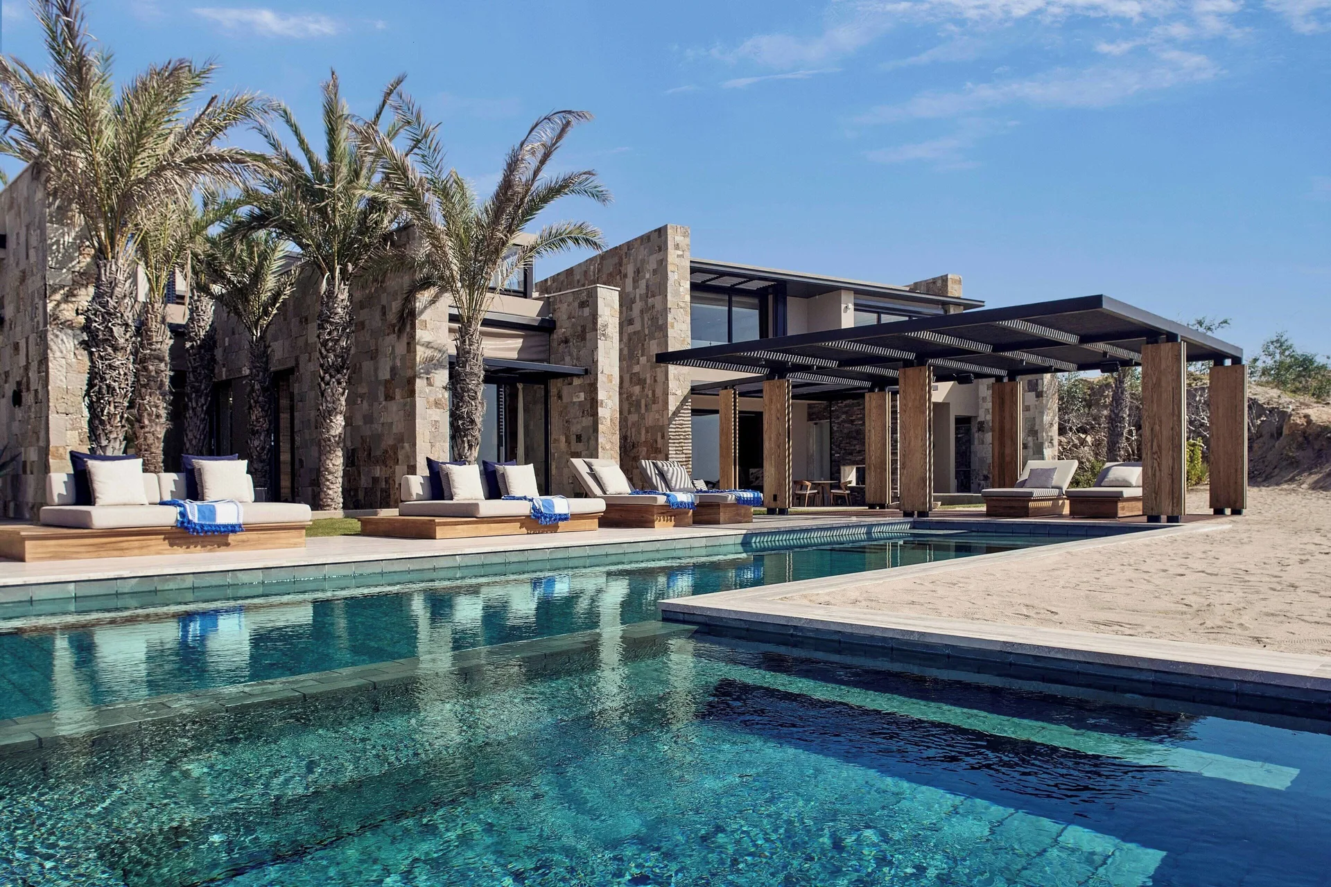 Resort pool with cabanas, palms, and stone buildings at Zadún, a Ritz-Carlton Reserve, Los Cabos.
