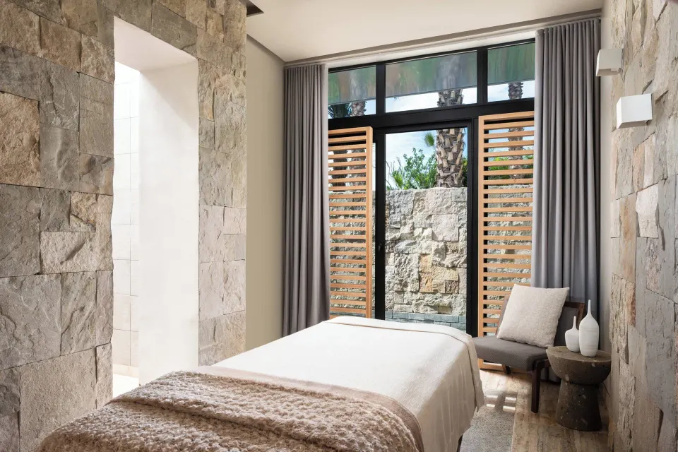 Spa treatment room with stone walls and garden doors at Zadún, a Ritz-Carlton Reserve, Los Cabos.