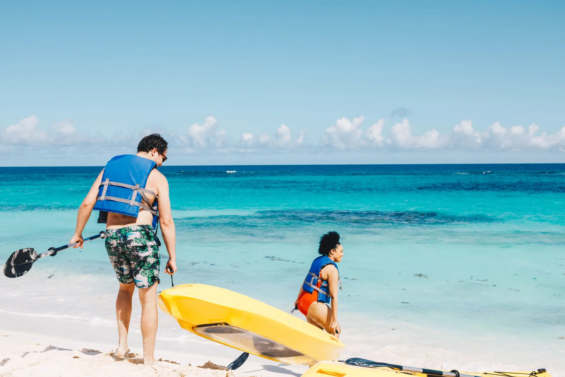 Guests carry kayaks into the turquoise surf at Zemi Beach House.