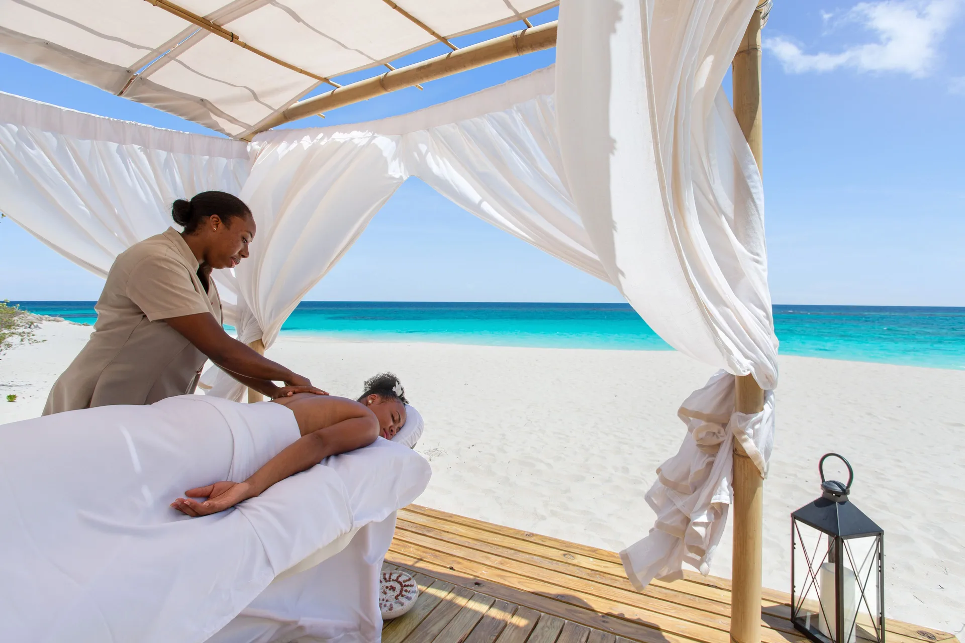 Beach massage under a white canopy beside turquoise water at Zemi Beach House.
