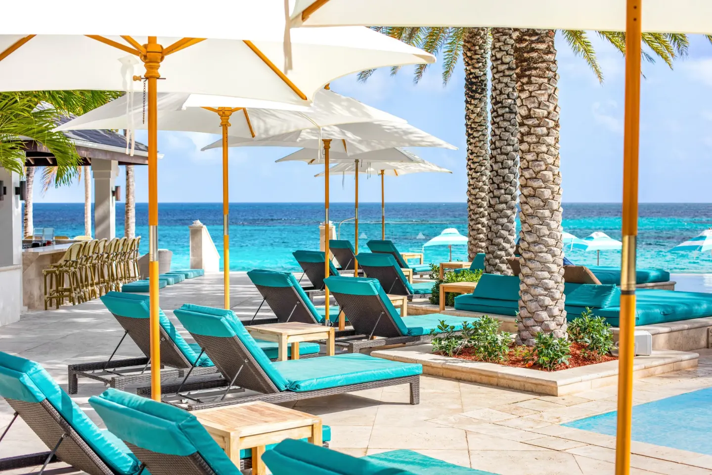 Beachfront pool deck with turquoise loungers, white umbrellas, and ocean views at Zemi Beach House.