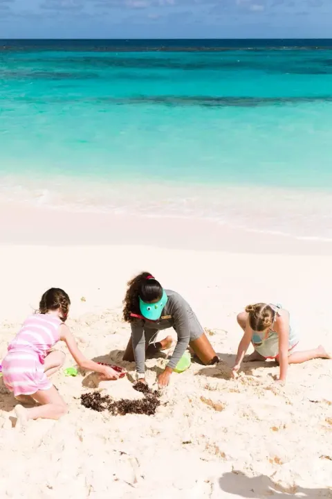 Children digging in white sand beside turquoise water at Zemi Beach House.