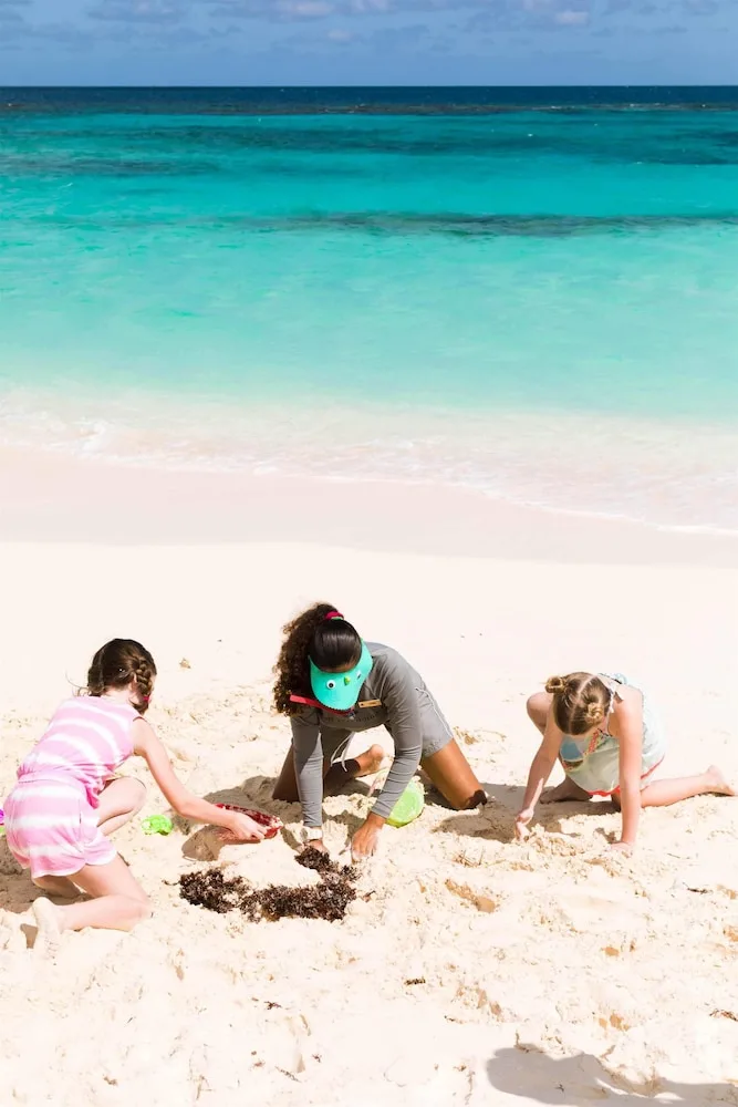 Children digging in white sand beside turquoise water at Zemi Beach House.