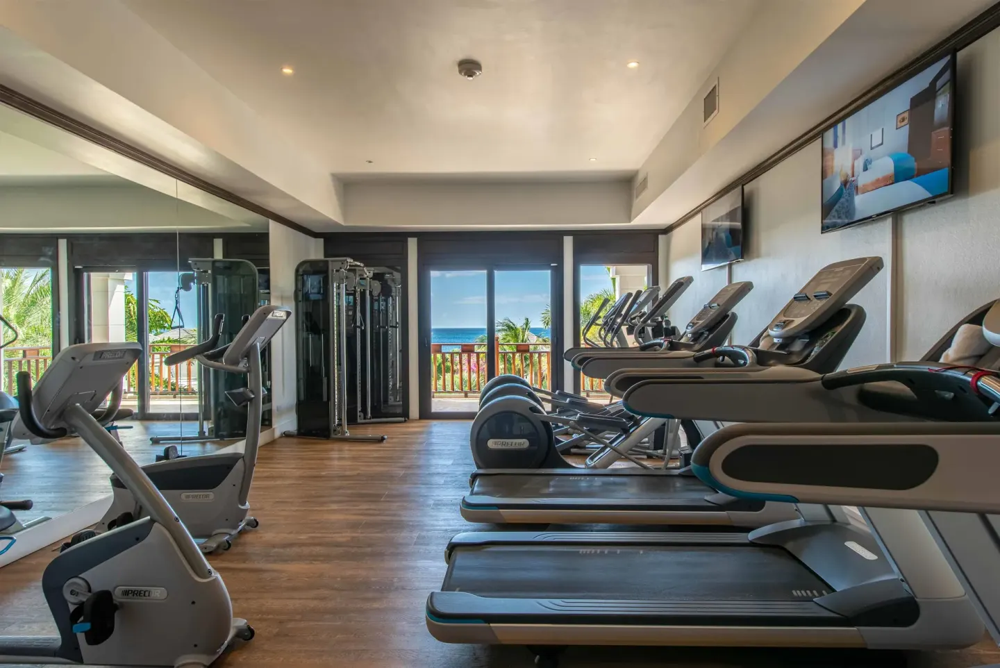 Fitness room with treadmills, exercise machines, mirrors, and ocean-facing doors at Zemi Beach House.