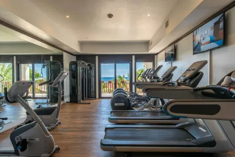 Fitness room with treadmills, exercise machines, mirrors, and ocean-facing doors at Zemi Beach House.