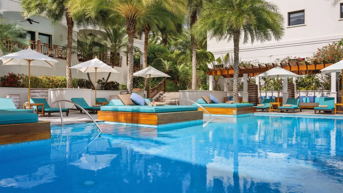 Palm-fringed resort pool with turquoise daybeds and umbrellas at Zemi Beach House.