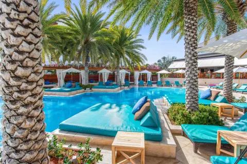 Resort pool with palm trees, cabanas, loungers, and turquoise cushions at Zemi Beach House.