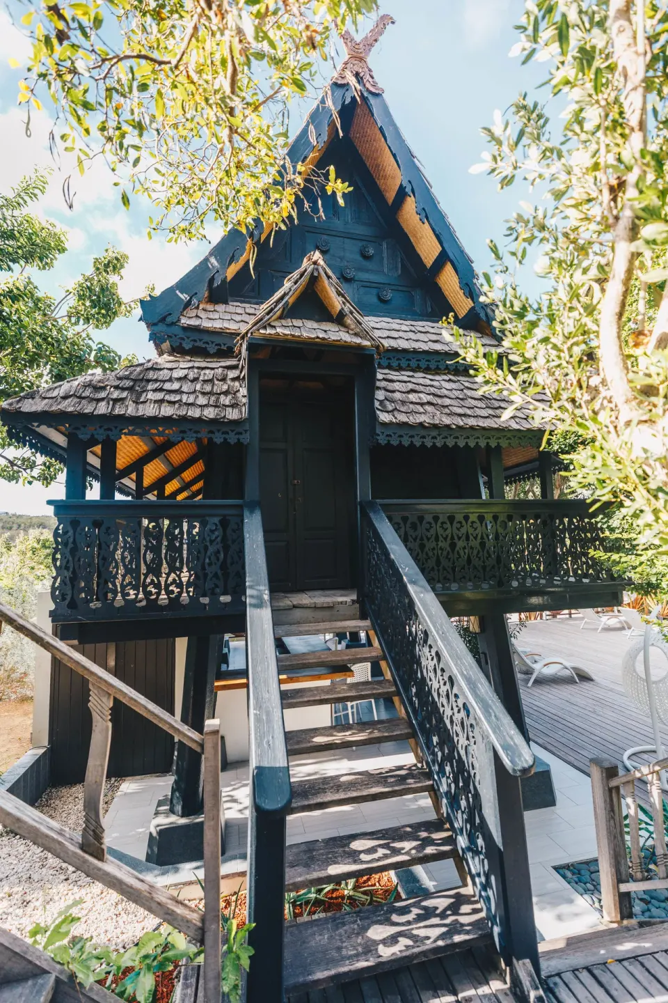 Dark wood spa house with carved railings and steps among trees at Zemi Beach House.
