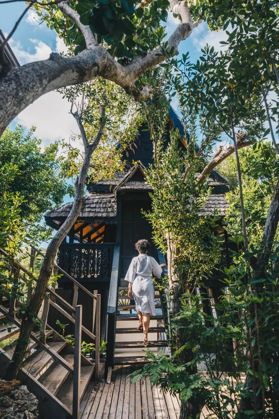 Guest in a robe walking through trees toward a spa house at Zemi Beach House.