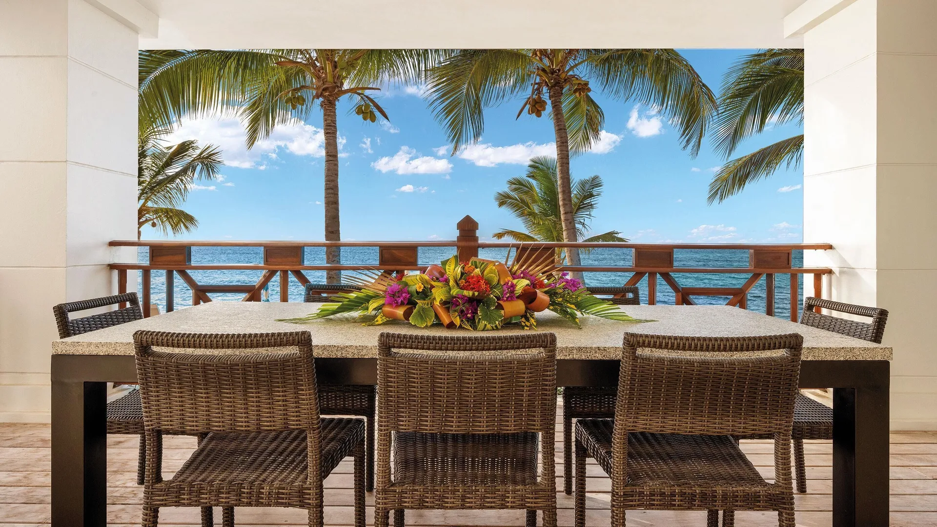 Covered oceanfront dining terrace at Zemi Beach House with wicker chairs and palm-framed sea views.