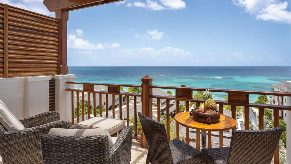 Ocean View room balcony with wicker seating, fruit, and turquoise sea at Zemi Beach House.
